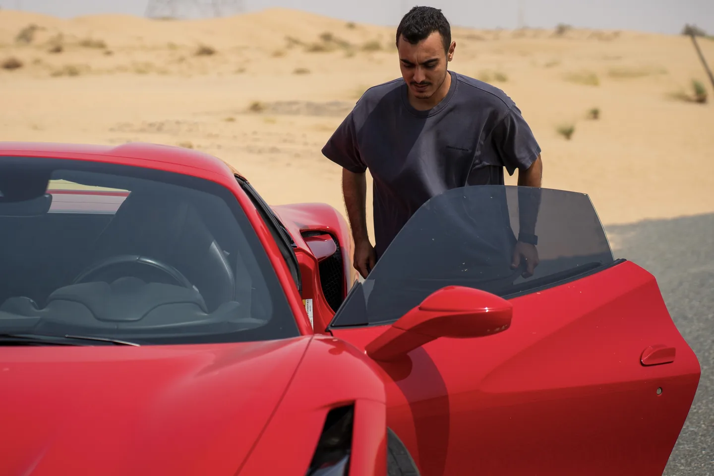 Basem Kamal standing beside a red Ferrari in the desert